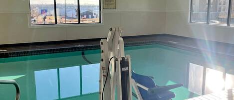 Una piscina interior con ventanas transparentes, un puesto de salvavidas y un cartel con las normas de la piscina.