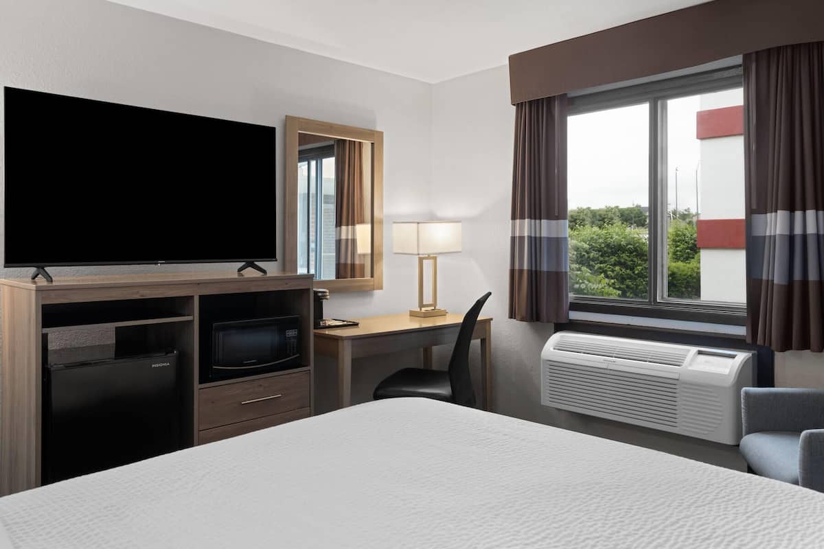Habitación de hotel con cama, escritorio con lámpara, televisor de pantalla plana, mini refrigerador, microondas y aire acondicionado.