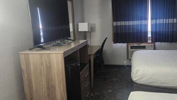 Ein Hotelzimmer mit einem Holztisch, einem Flachbildfernseher, einem Sessel, einem Bett und einem Fenster mit Vorhängen.