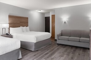 Ein Hotelzimmer mit einem Doppelbett, einem grauen Sofa, einem Holz-Kopfteil, einem Nachttisch mit Lampe und einer Wandleuchte.