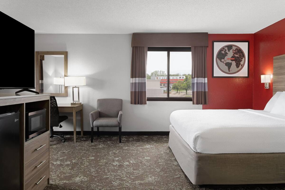 Habitación de hotel con cama, escritorio con computadora, televisor y vista al exterior.