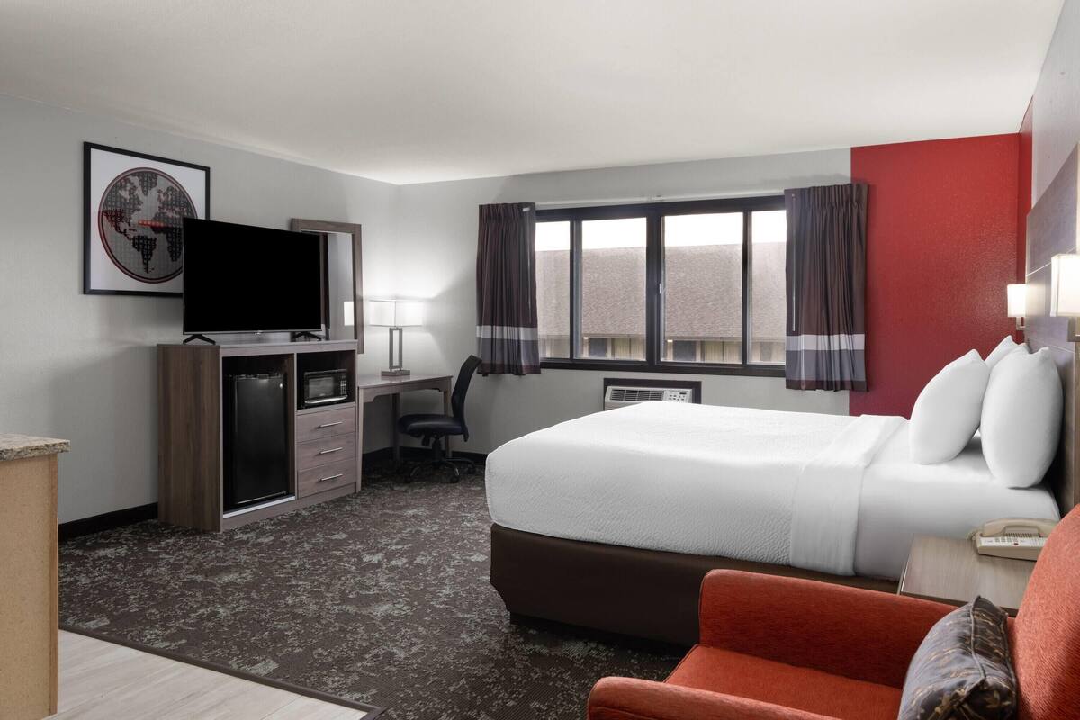 Una habitación de hotel con una cama, un escritorio con computadora, un televisor y una ventana con cortinas.