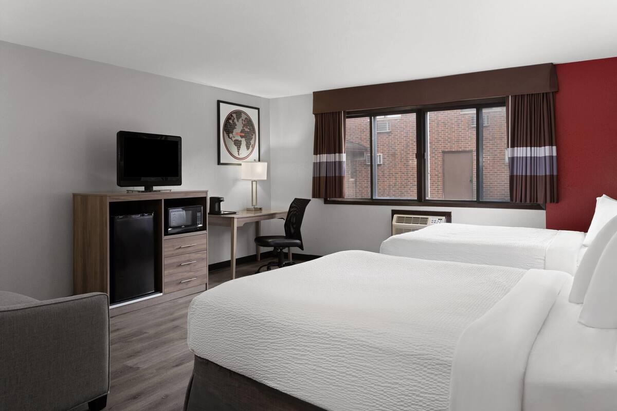 Habitación de hotel con dos camas, un escritorio con computadora, televisor y ventana con cortinas.
