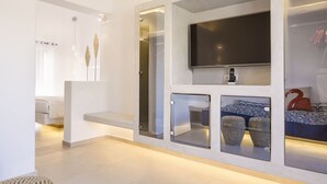Une chambre d’hôtel moderne dotée d’un grand téléviseur à écran plat fixé au mur, d’une banquette intégrée et d’un coin salon agrémenté de paniers décoratifs.