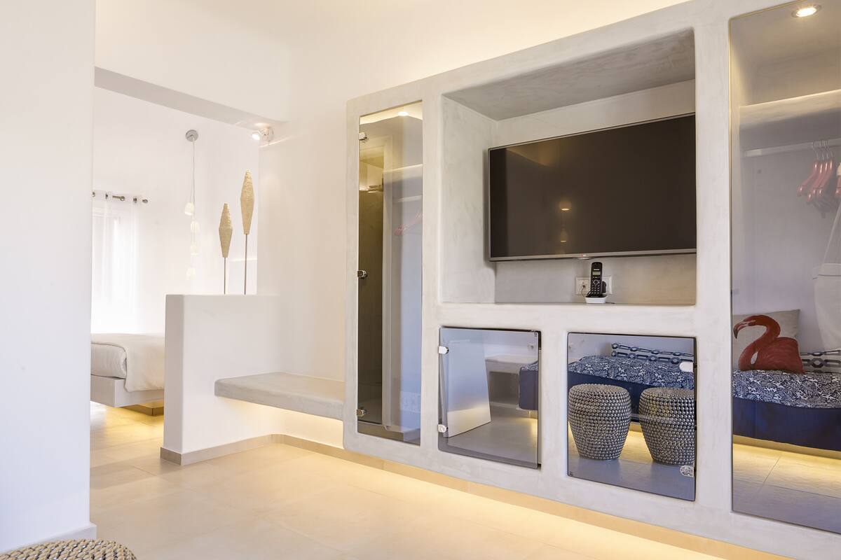 Une chambre d’hôtel moderne dotée d’un grand téléviseur  à écran plat fixé au mur, d’une banquette intégrée et d’un coin salon agrémenté de paniers décoratifs.