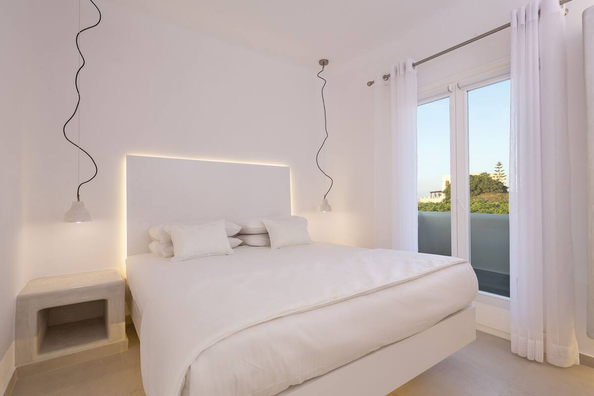 Une chambre moderne avec un grand lit, une table de chevet et une vue sur un balcon.