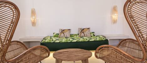 A room with a green sofa, two wicker chairs, a round wooden table, and two wall-mounted lights.