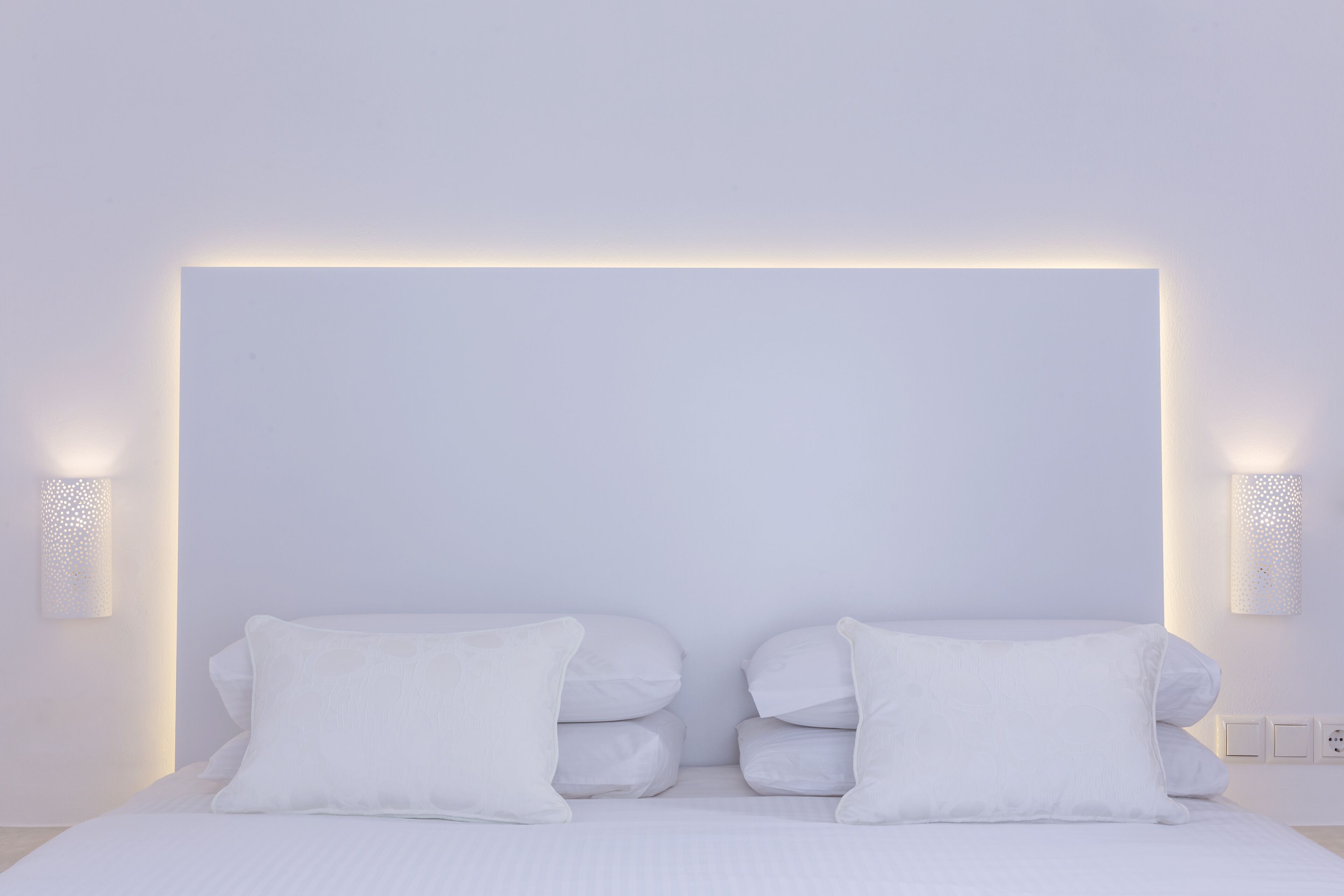 A modern bedroom with a large bed, white bedding, and wall-mounted lighting.
