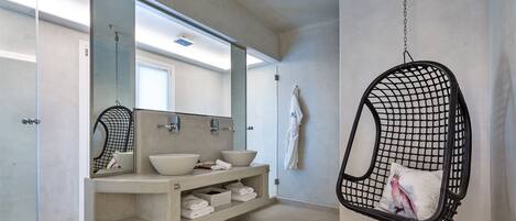 A modern bathroom with a glass shower enclosure, a double sink vanity, and a hanging chair with a cushion.