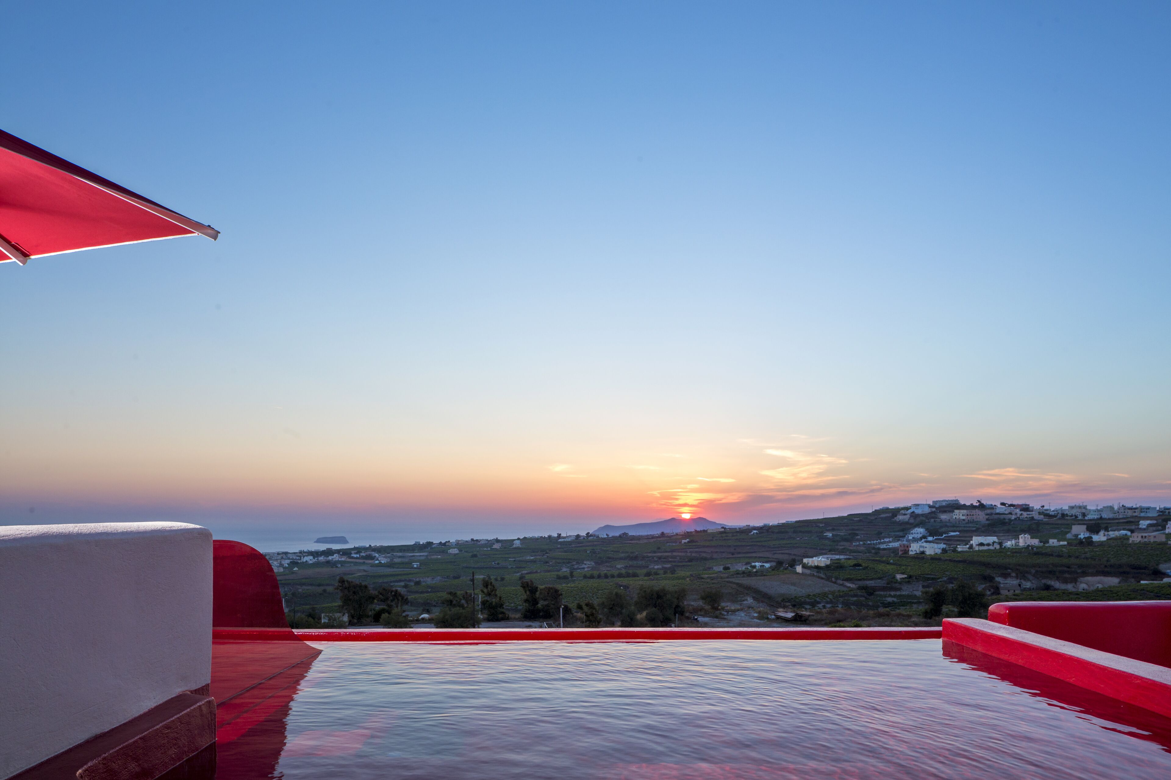 A rooftop pool with a sunset view, red railings, and a clear sky.
