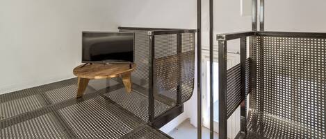 Une pièce avec une table en bois, une chaise en métal noir et un téléviseur posé sur un meuble.