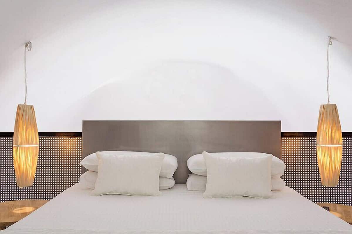 A modern hotel room with a large bed, two bedside lamps, and a large wall-mounted headboard.