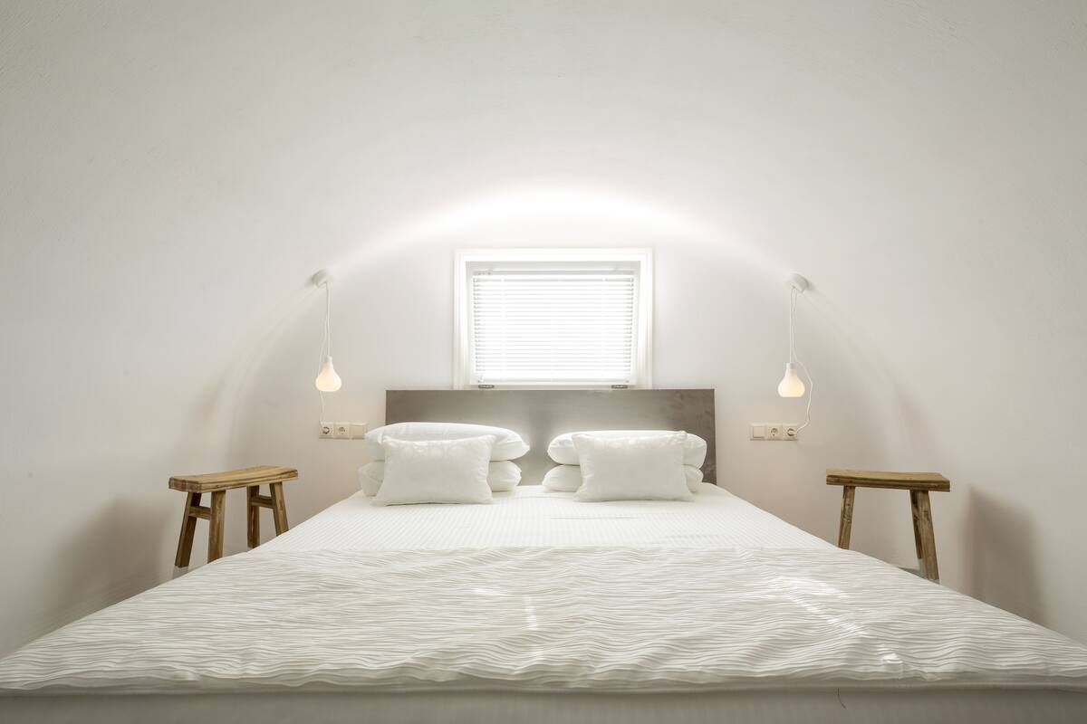 Une chambre à coucher comprenant un lit, deux tables de chevet, une fenêtre et des luminaires fixés au mur.