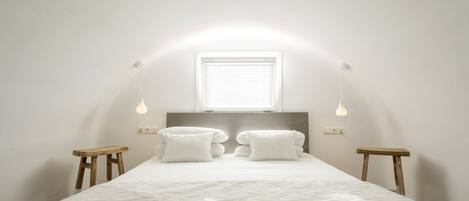 Un dormitorio con cama, dos mesitas de noche, una ventana e iluminación en la pared.