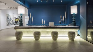 Un espace d'accueil avec un mur bleu, un comptoir de réception et trois tabourets à l'assise texturée.