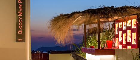 Un bar llamado "Bloody Mary Pool" con techo de paja y vistas a las montañas.