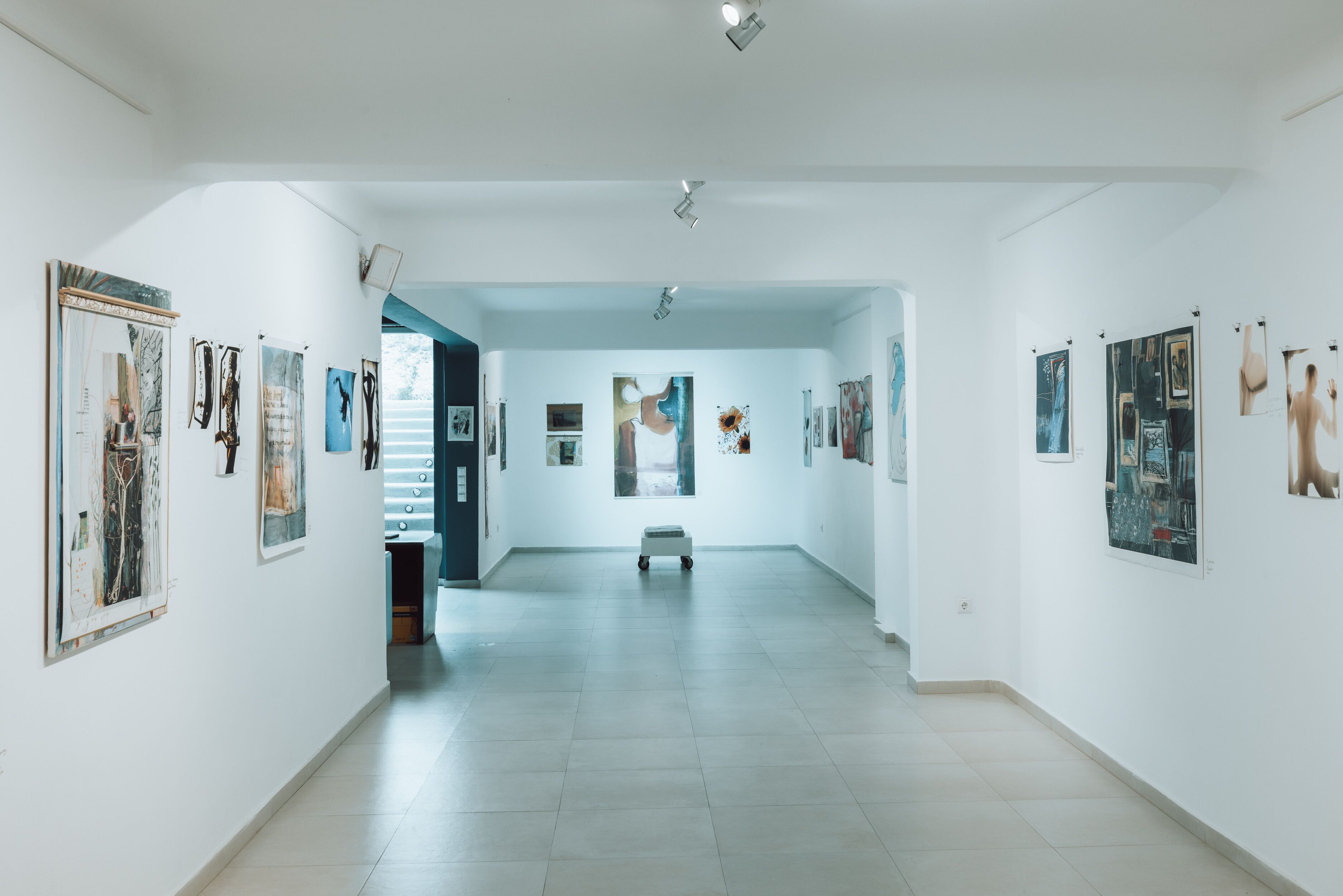 A gallery with artworks on the walls, a central bench, and a tiled floor.