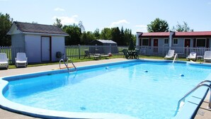 En rektangulär swimmingpool med en vit kant runt om, omgiven av ett vitt staket och ett litet förråd till vänster.