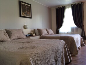 A hotel room with two beds, a bedside table with a lamp, a framed picture on the wall, and a window with curtains. - Motel de la Pente Douce (Magog)