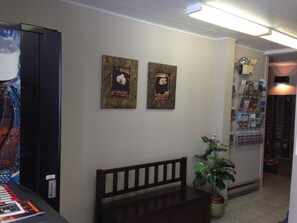 A room with a piano, a bench, two framed artworks, a potted plant, and a bookshelf with books and magazines. - Motel de la Pente Douce (Magog)