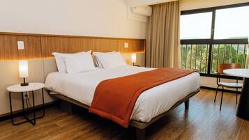 A hotel room with a bed, two bedside tables, a chair, a small table, and a window with a view.