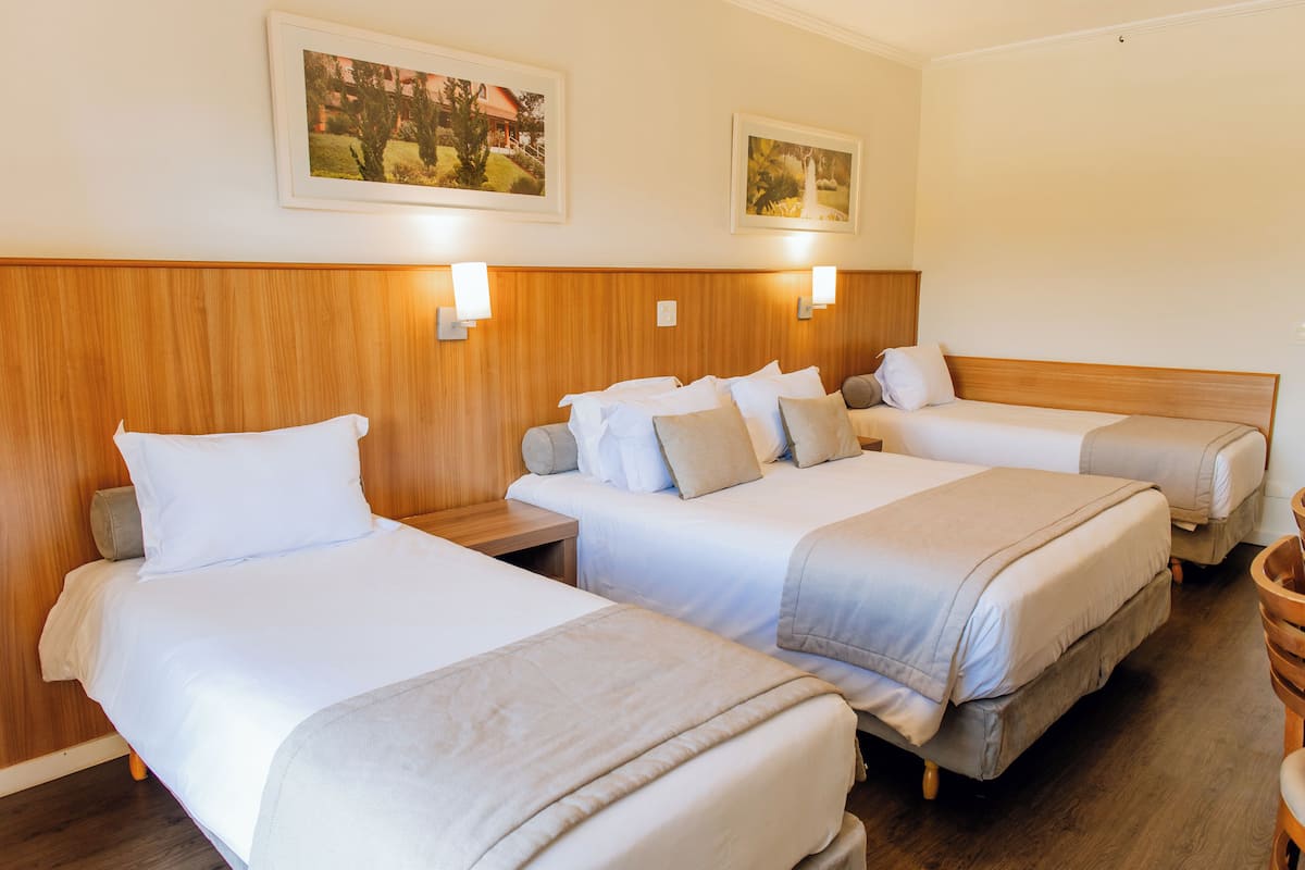 Ein Hotelzimmer mit drei Einzelbetten, Holz-Kopfteilen, Nachttischen und Wandleuchten.