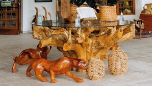 Una mesa de centro de madera con superficie de vidrio, rodeada de objetos decorativos y una planta en maceta.