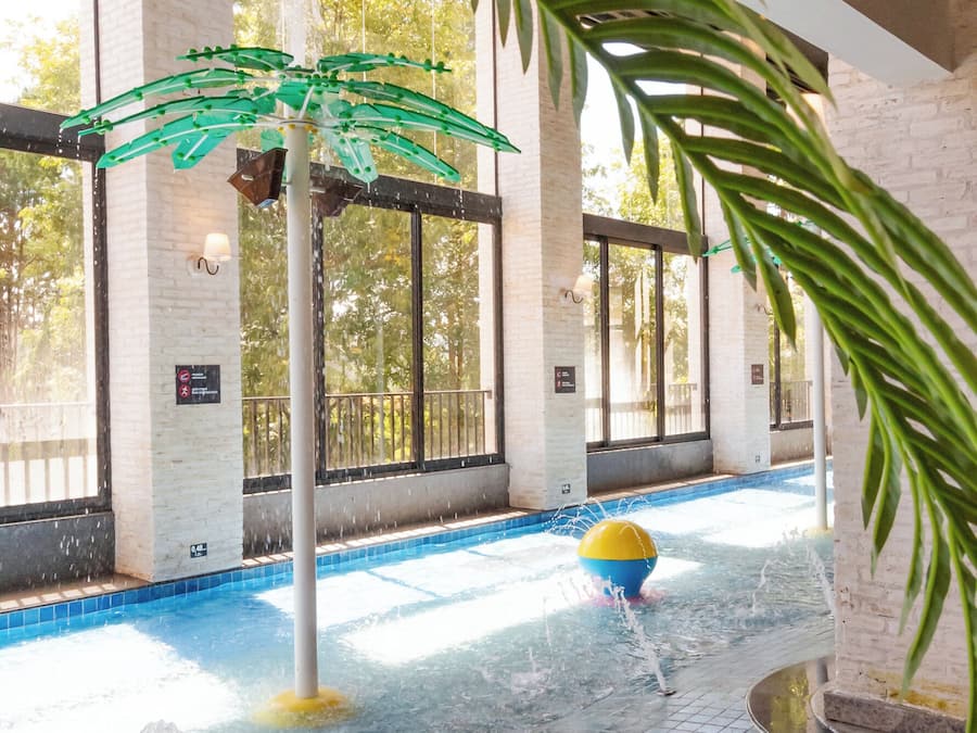Una piscina interior con una fuente acuática, rodeada de muros de ladrillo y grandes ventanales.
