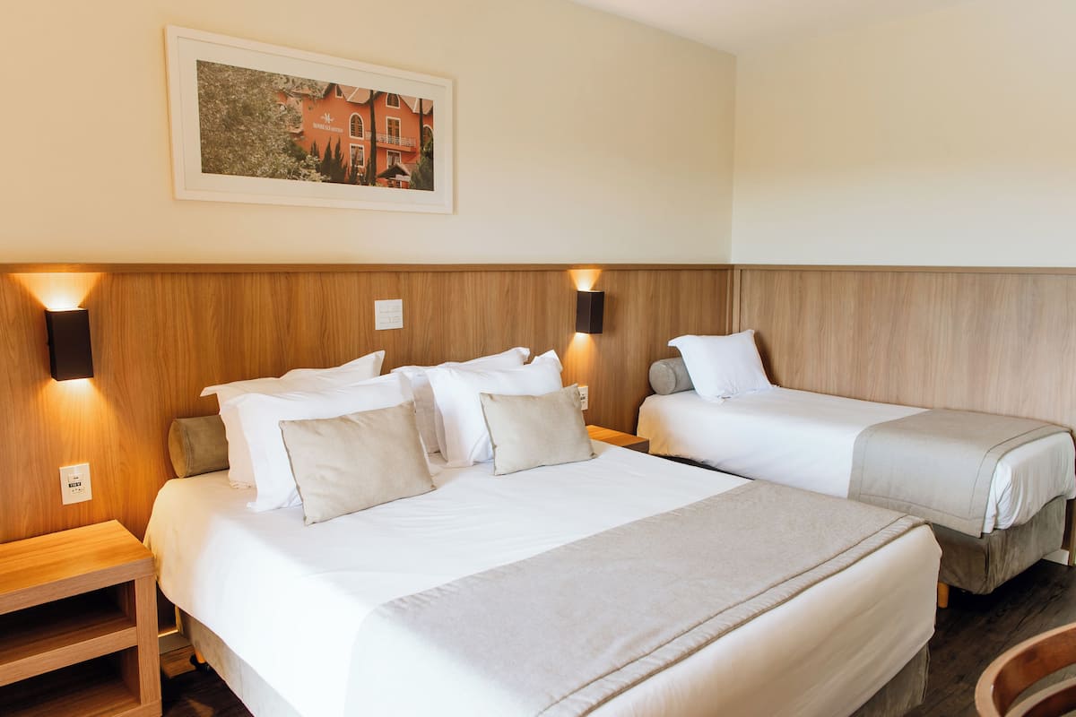 Ein Hotelzimmer mit zwei Betten, Holz-Kopfteilen, Nachttischlampen, einem gerahmten Bild an der Wand und einem kleinen Nachttisch.