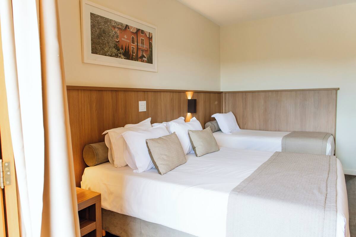 Ein Doppelbett mit weißen Laken und beigen Kissen, ein Holzkopfstück, ein kleiner Nachttisch und ein gerahmtes Bild an der Wand.