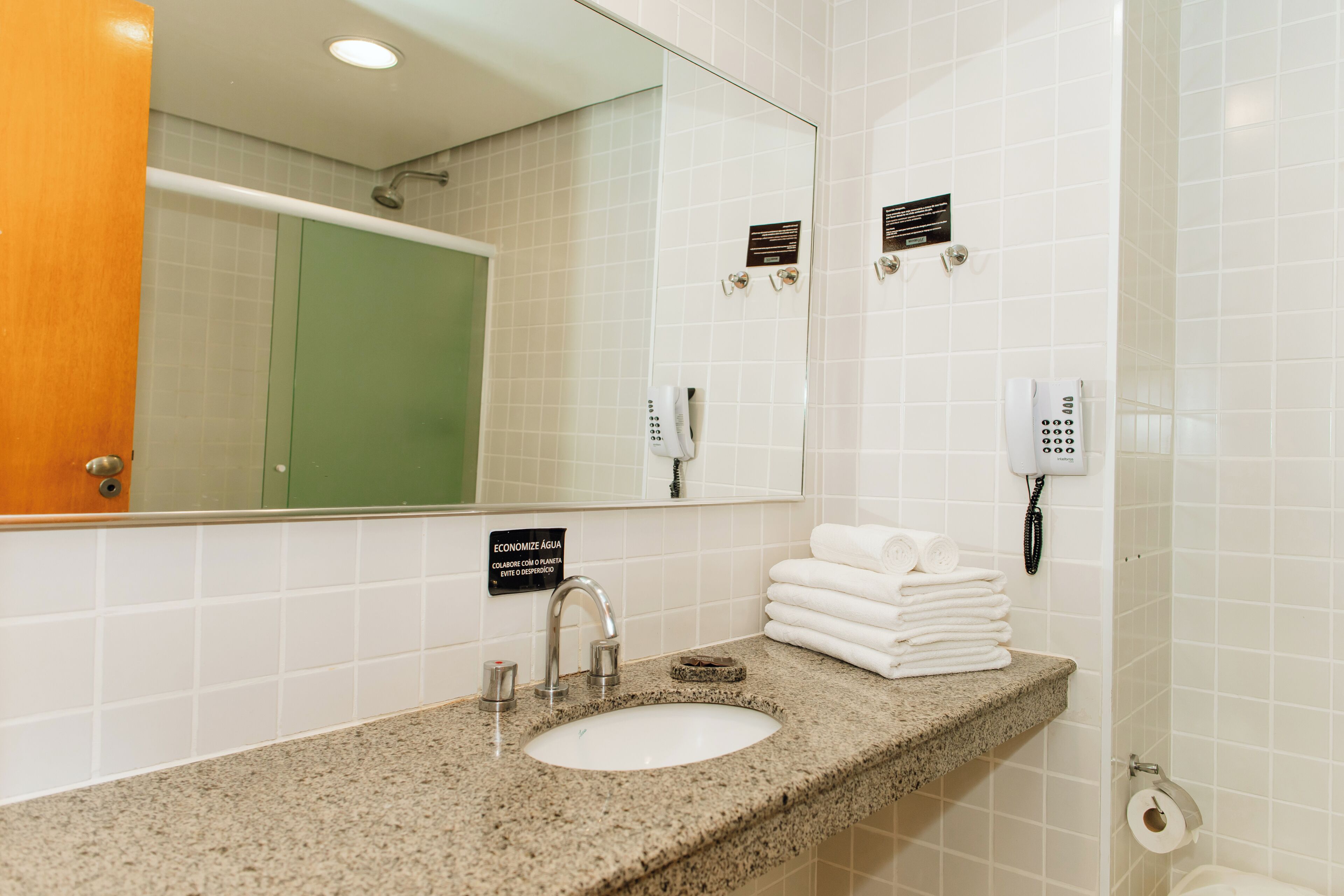 Baño de hotel con lavamanos, espejo, toallero y dos teléfonos.