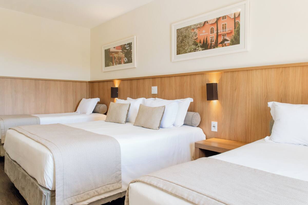 Ein Hotelzimmer mit drei Betten, Holz-Kopfteilen und zwei gerahmten Bildern an der Wand.
