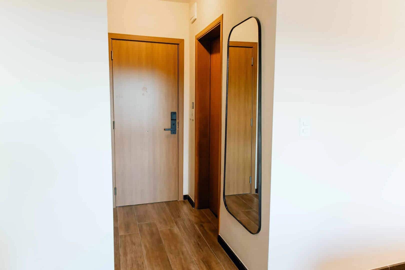 A hallway with a wooden door, a mirror, and a light switch on the wall.