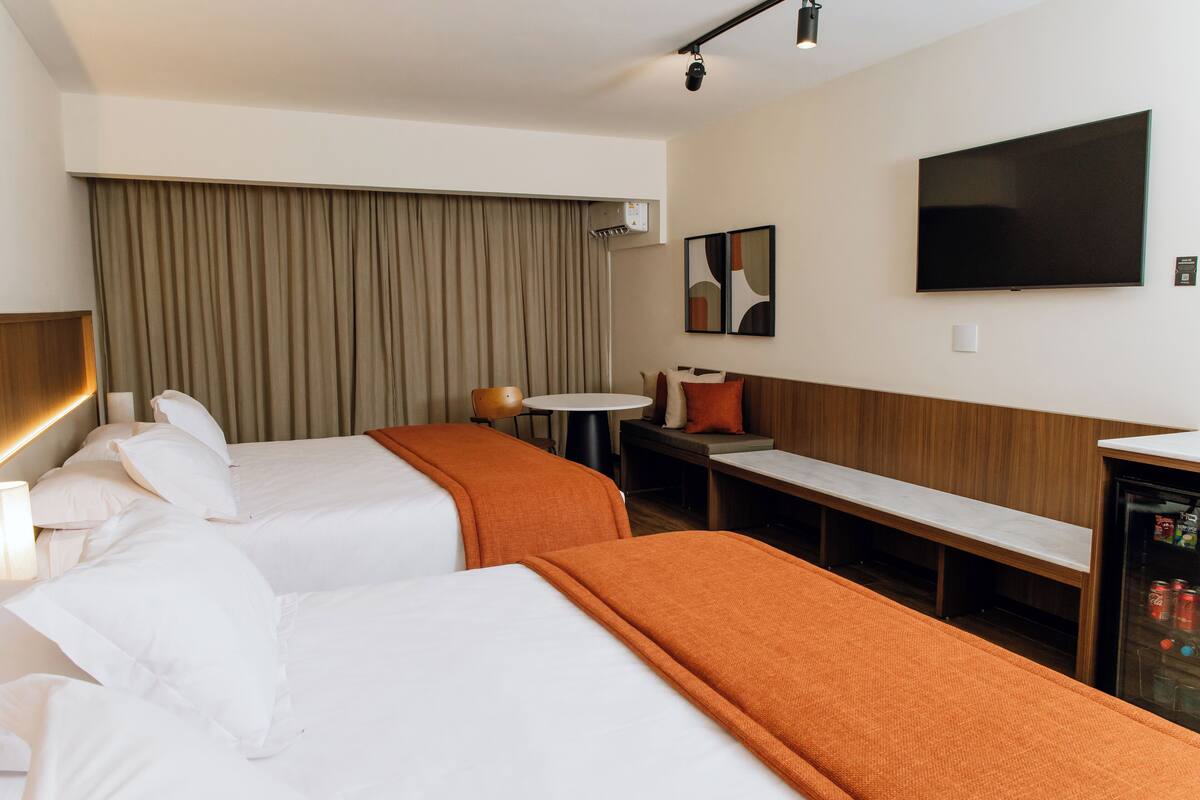 Ein Hotelzimmer mit zwei Betten, einem Schreibtisch, einem Fernseher und einer Minibar.