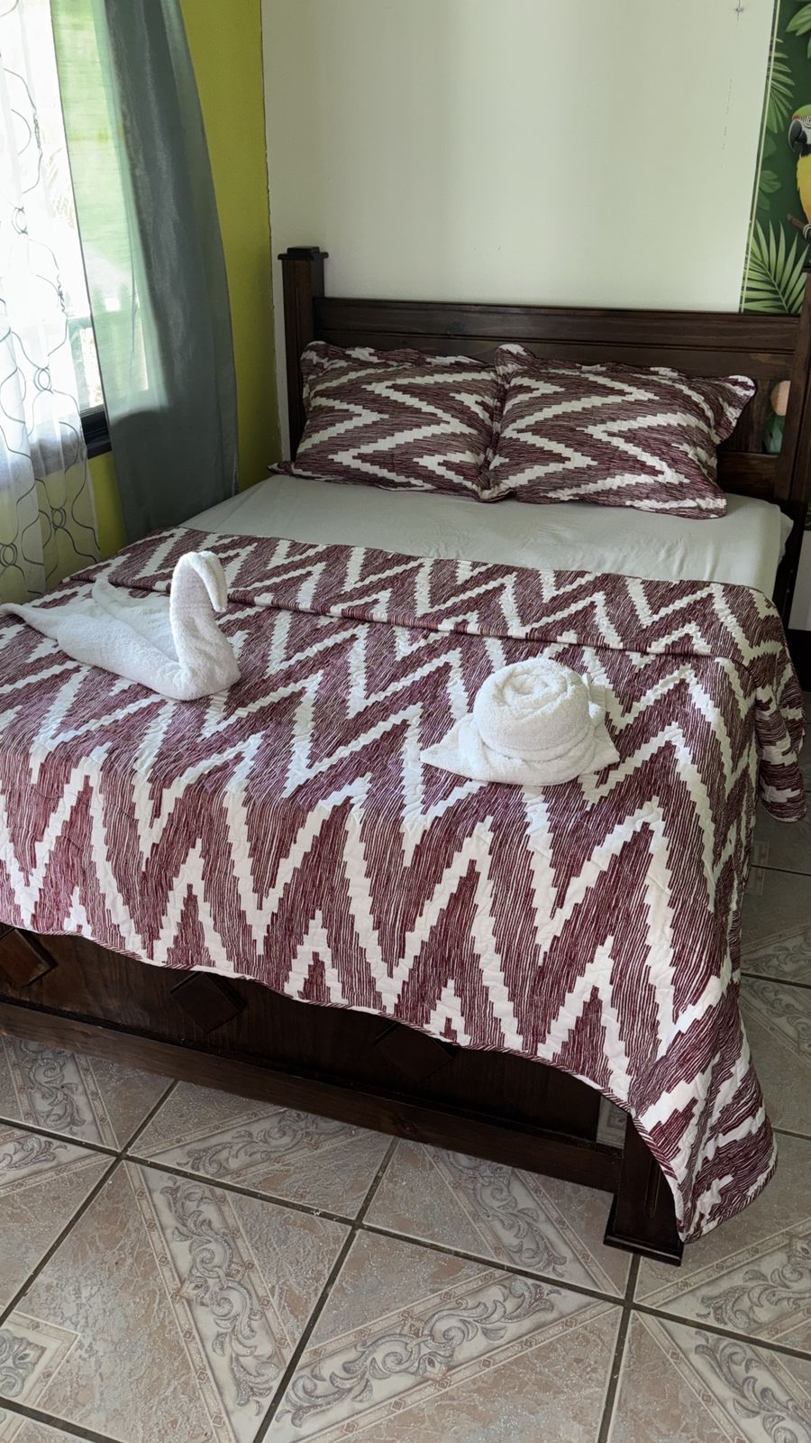 A bed with a patterned bedspread and pillows, a wooden headboard, and a decorative mirror.