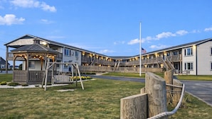 A multi-story hotel with a covered outdoor seating area, a flagpole, and a well-maintained lawn. - Mariner's Point Resort (Falmouth)