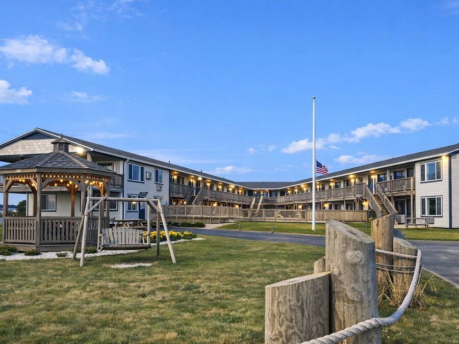 A multi-story hotel with a covered outdoor seating area, a flagpole, and a well-maintained lawn.