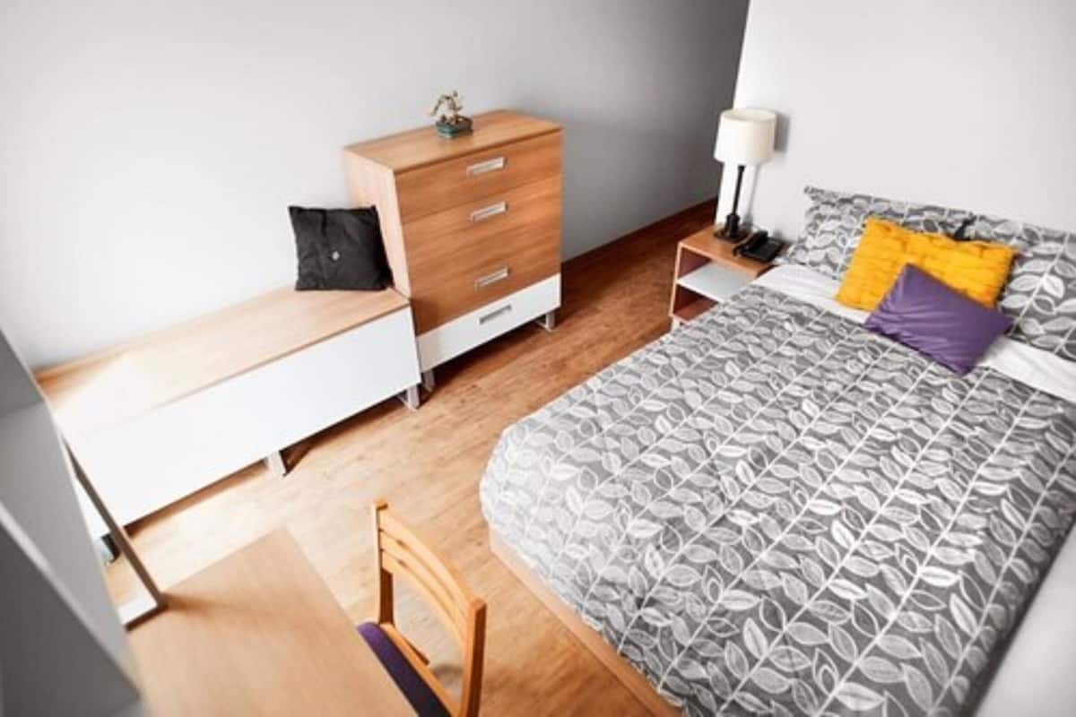 A bedroom with a bed, a wooden dresser, a nightstand, a chair, and a desk.