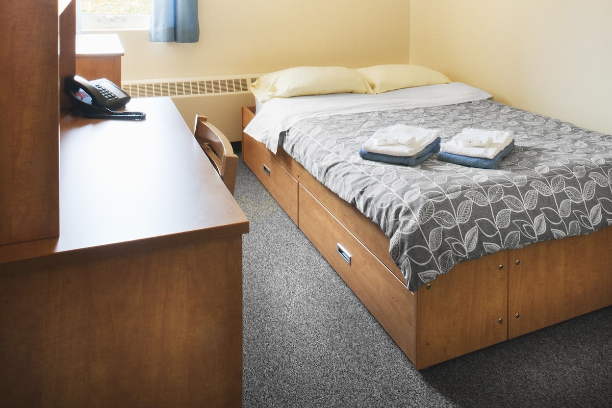 A bedroom with a bed, a desk, a telephone, and a window with curtains.