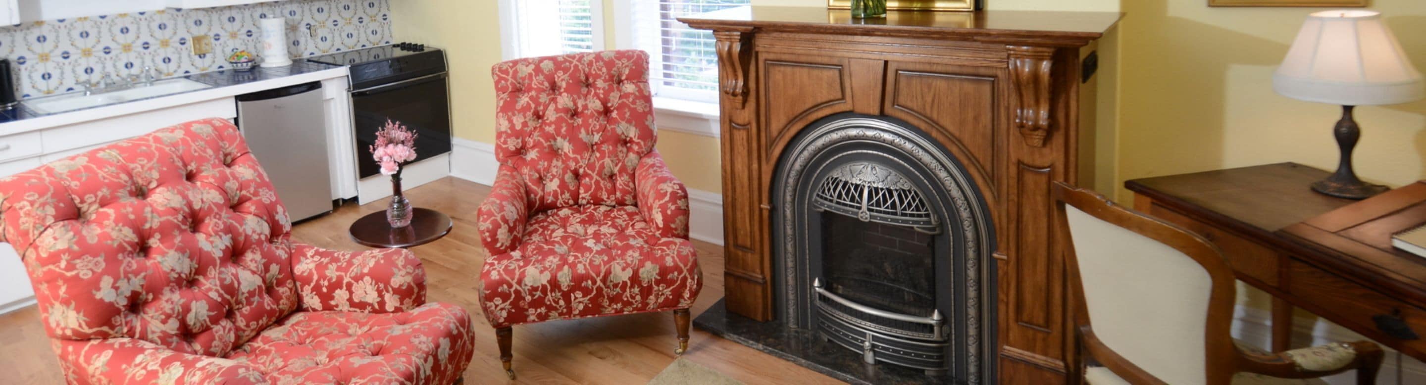 A living room with a fireplace, floral armchairs, a wooden cabinet, and a lamp.