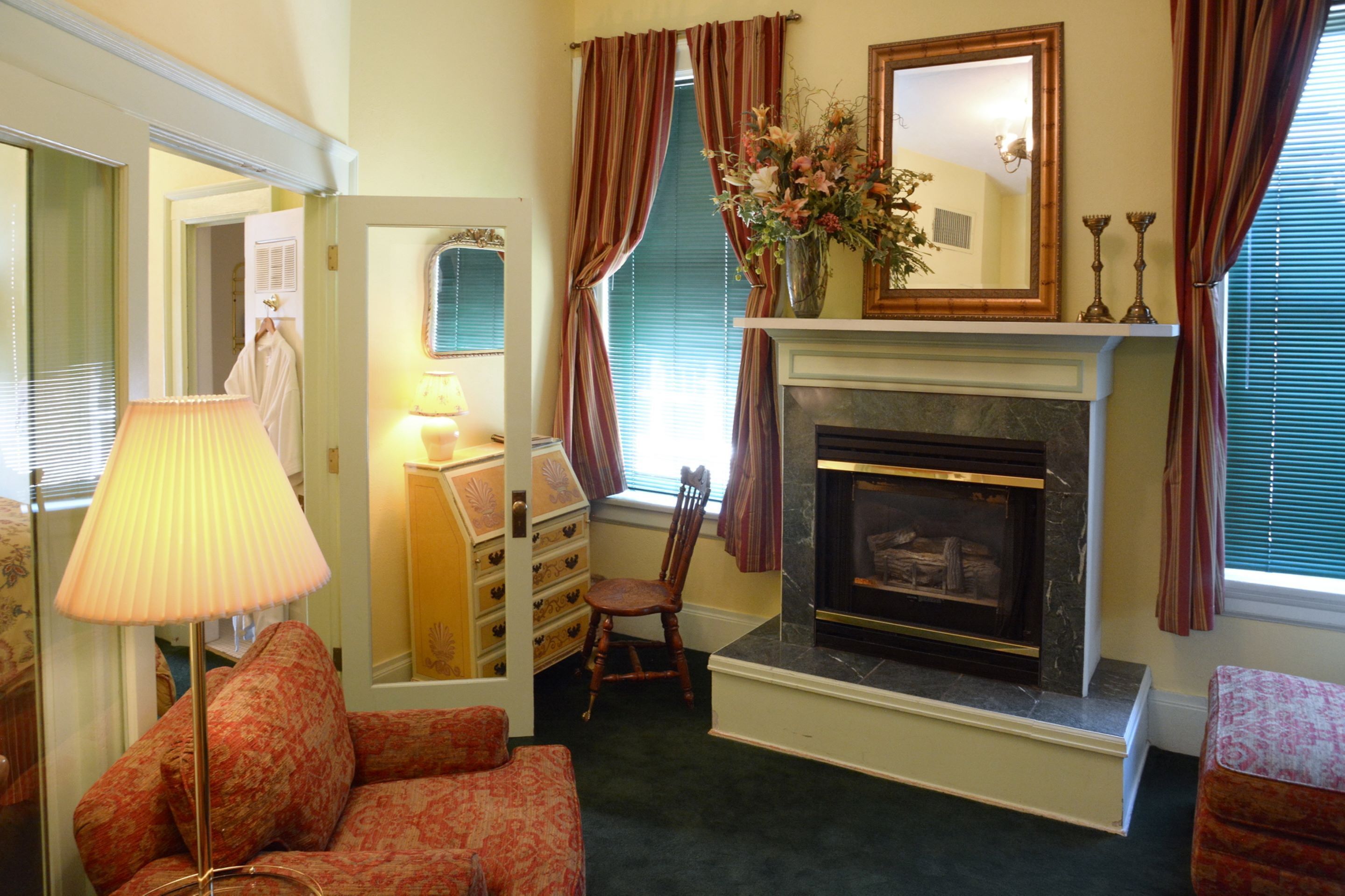 A living room with a fireplace, a lamp, a chair, and a dresser.