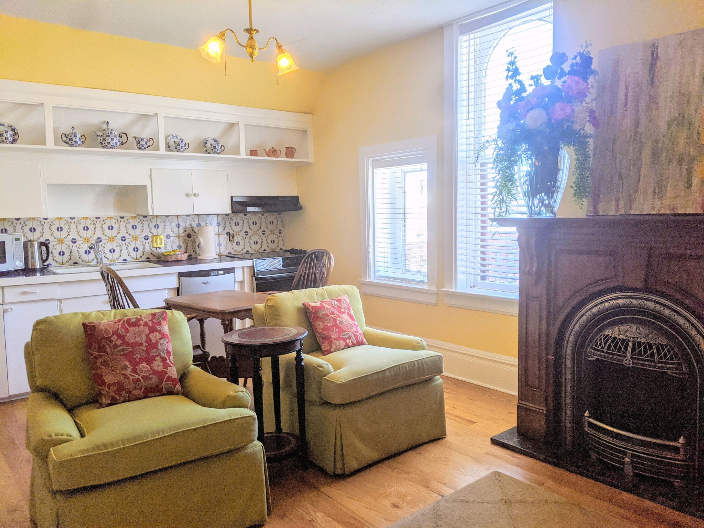 A cozy living room with a fireplace, a dining area, and a kitchen with white cabinets and patterned tiles.