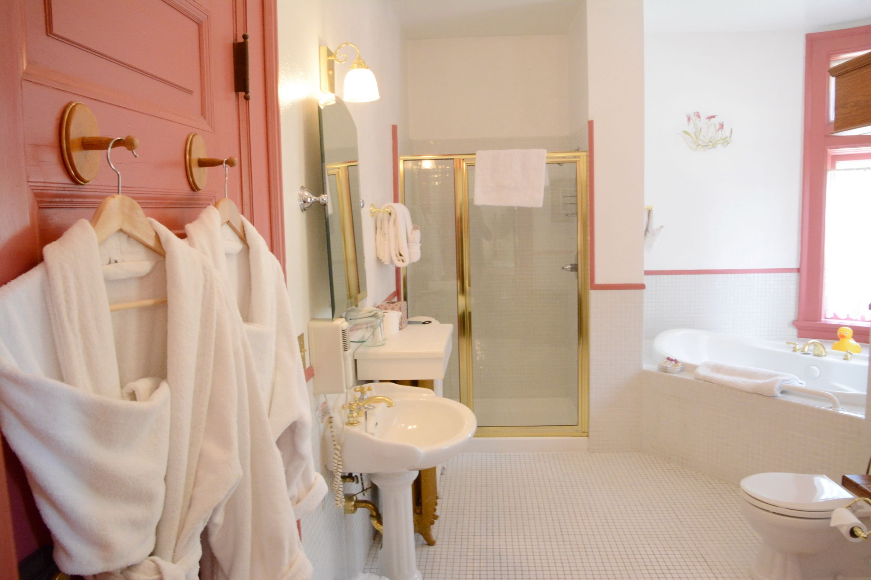 Un baño con tocador rosa, lavamanos blanco y ducha con mampara de vidrio.