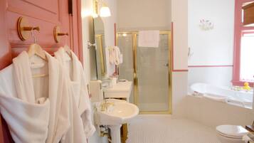 Un baño con tocador rosa, lavamanos blanco y ducha con mampara de vidrio.