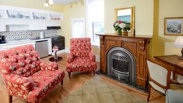 Una sala de estar con chimenea, una mesa de comedor y una zona de cocina con armarios blancos y salpicadero de azulejos.