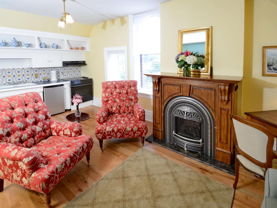 Una sala de estar con chimenea, una mesa de comedor y una zona de cocina con armarios blancos y salpicadero de azulejos.