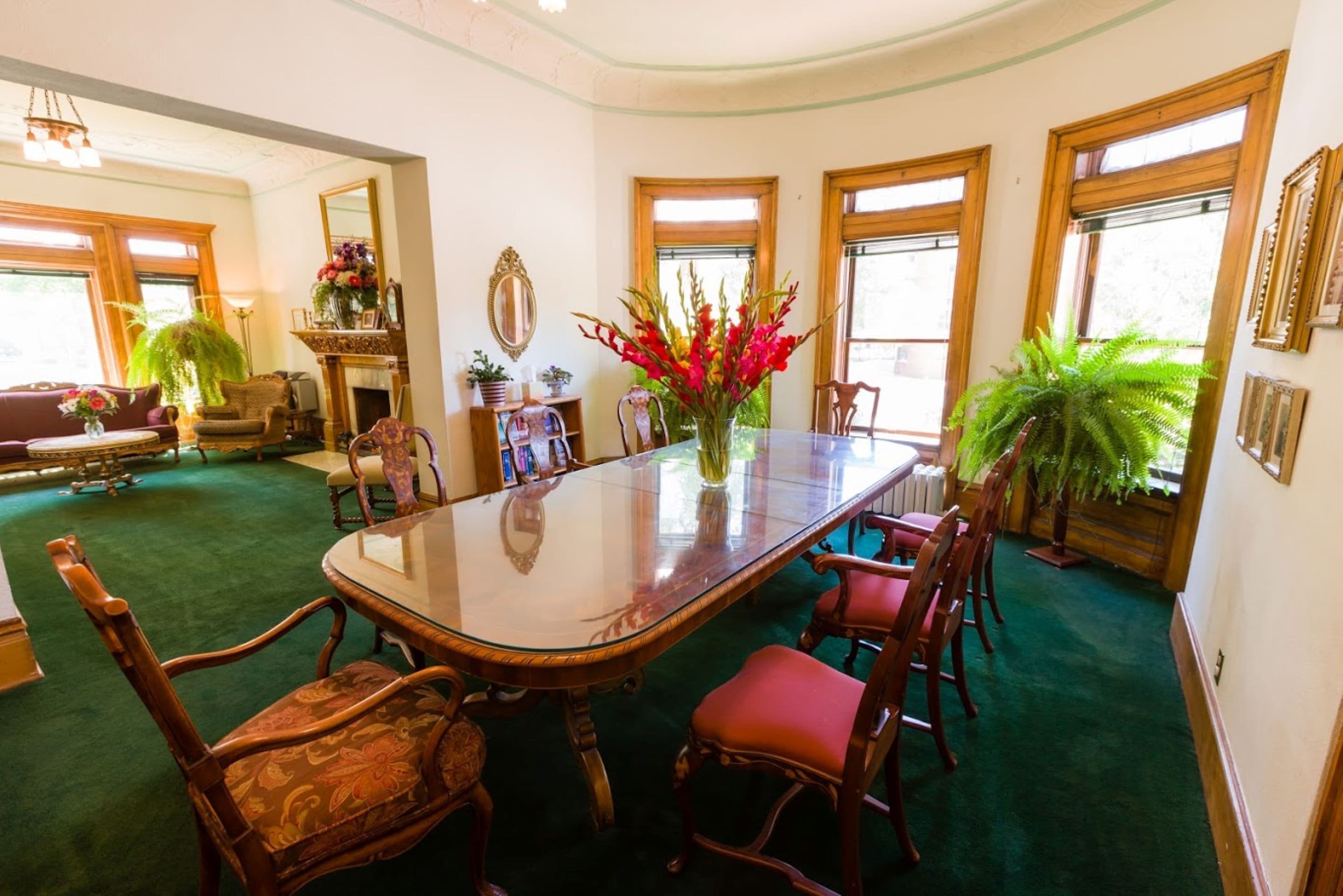 A dining area with a glass-top table, wooden chairs, and potted plants.