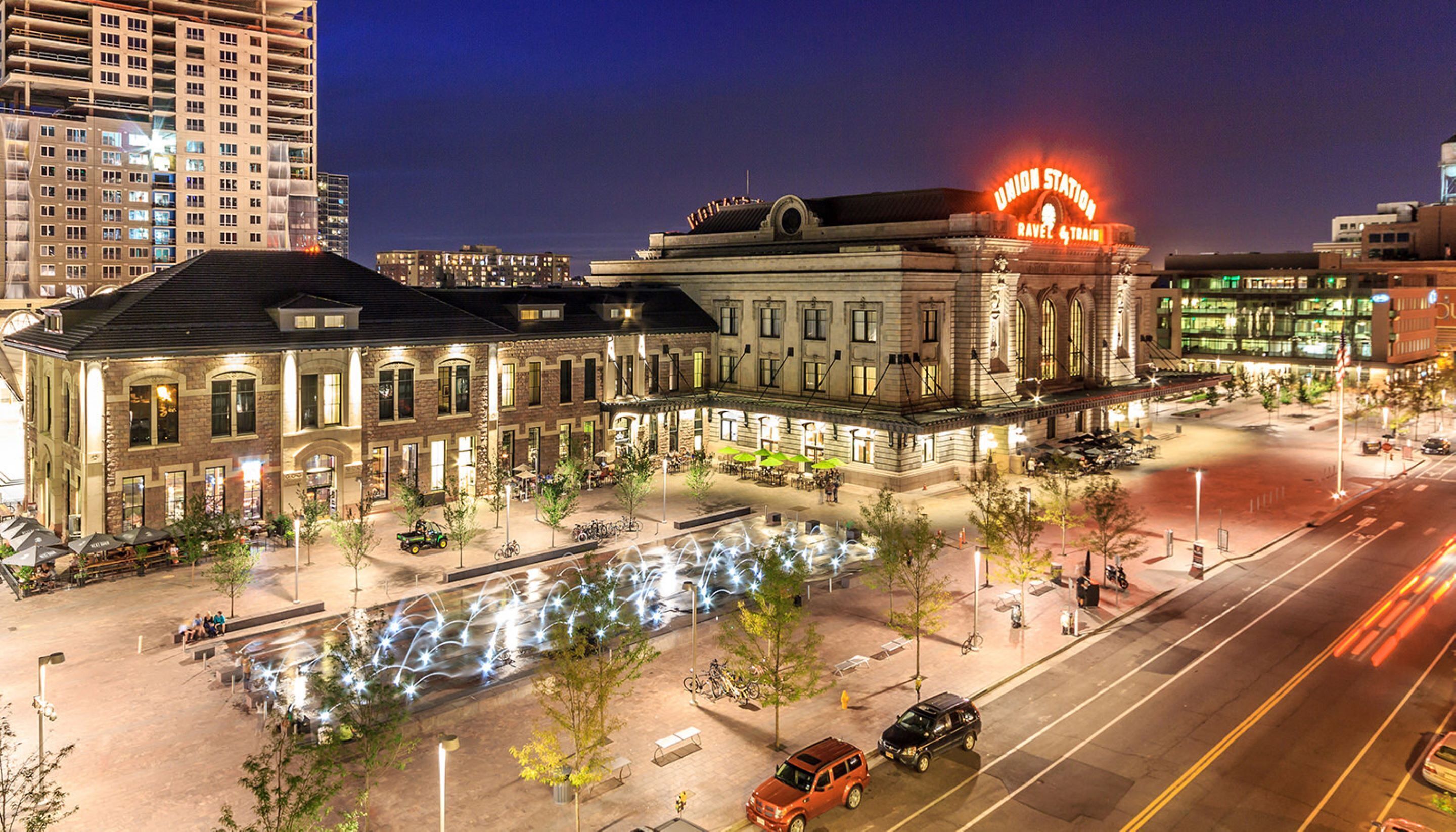 A historic building with a prominent neon sign, outdoor seating, and a well-lit plaza.