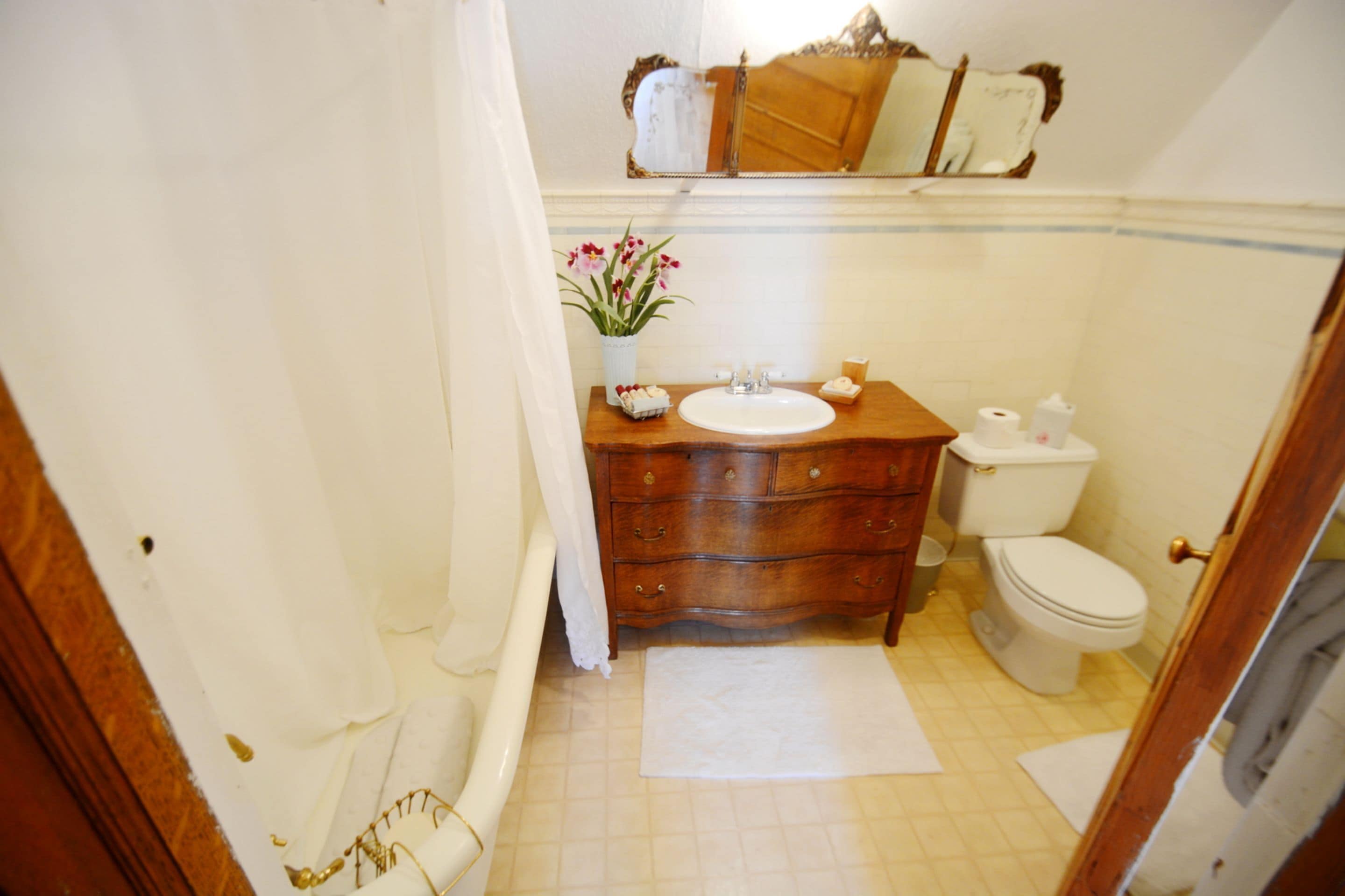Un baño con tocador de madera, lavamanos blanco y retrete.