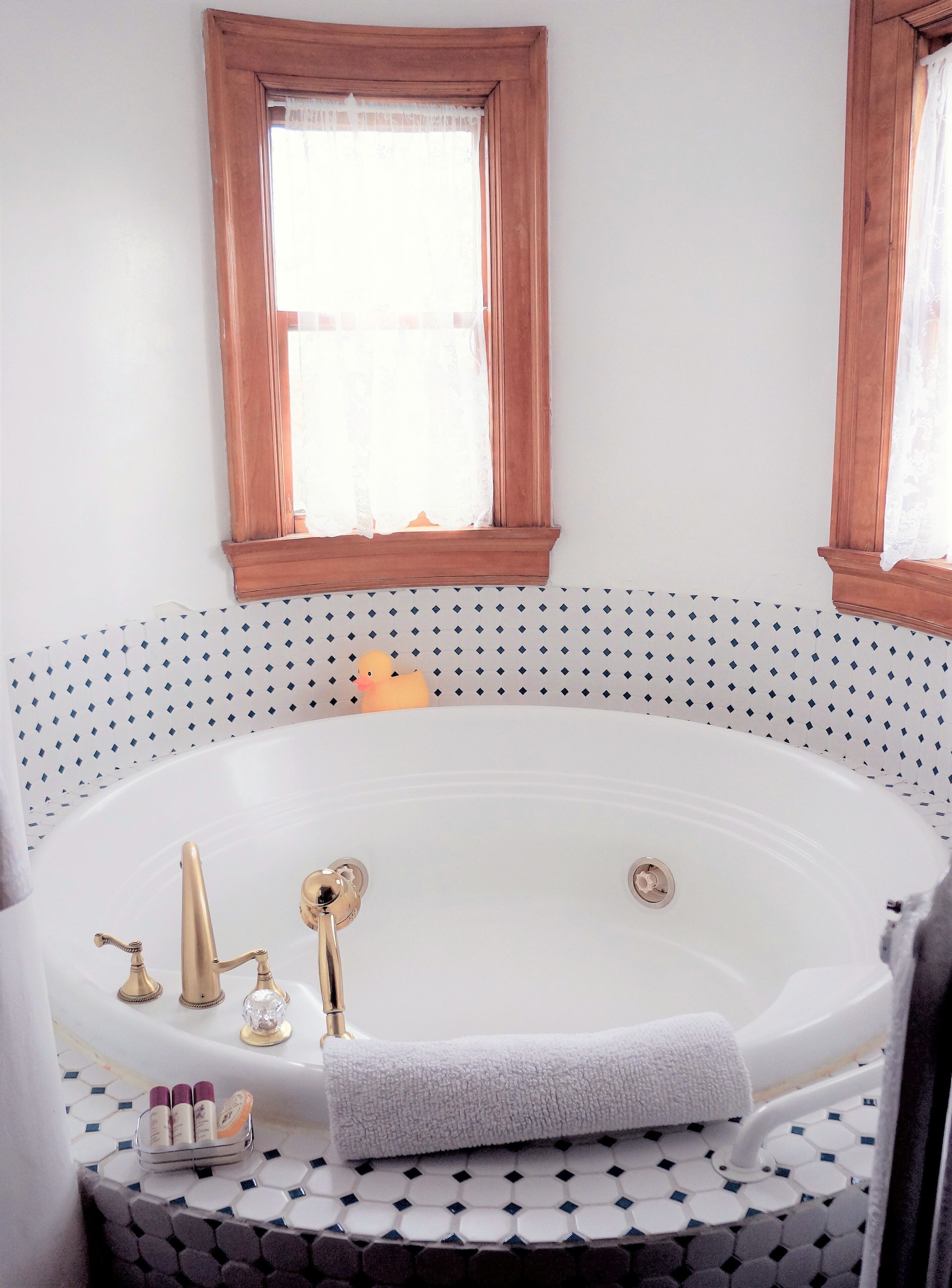 A bathroom with a freestanding bathtub, a window with wooden trim, and a patterned tile backsplash.